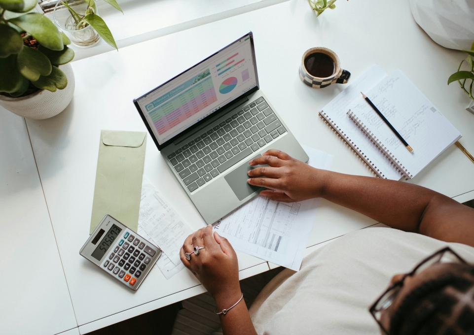 person sitting at desk with computer, calculator, coffee, and notebook